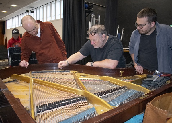(centre) Steve Droy, professional concert piano tuner and founder of the Piano Technology School, works on the baby grand piano at the Benn Hall with students Eoin McCarthy (left) and Henry Melbourne (right).